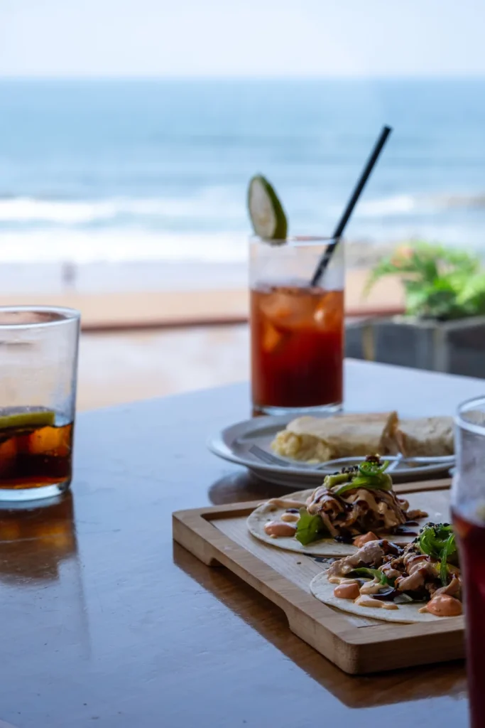 Tacos and iced drinks on a table beside a beach