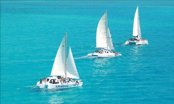 Three catamarans sailing across turquoise Caribbean water