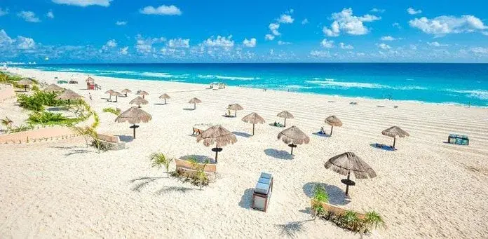 Praia de Cancún com guarda-sóis de palha e mar turquesa.