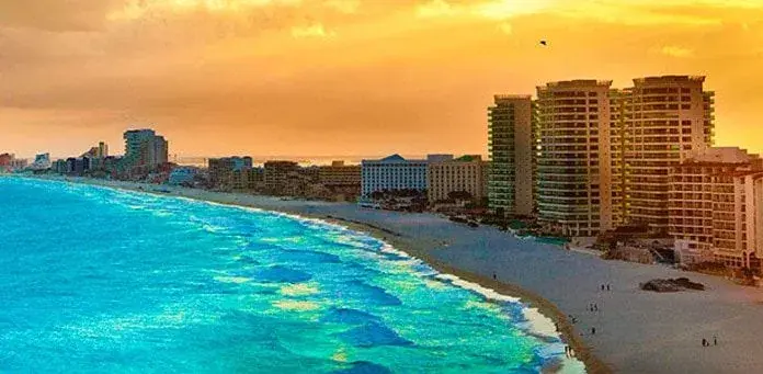 Hoteles frente a la playa en Cancún bajo un cielo dorado al atardecer.