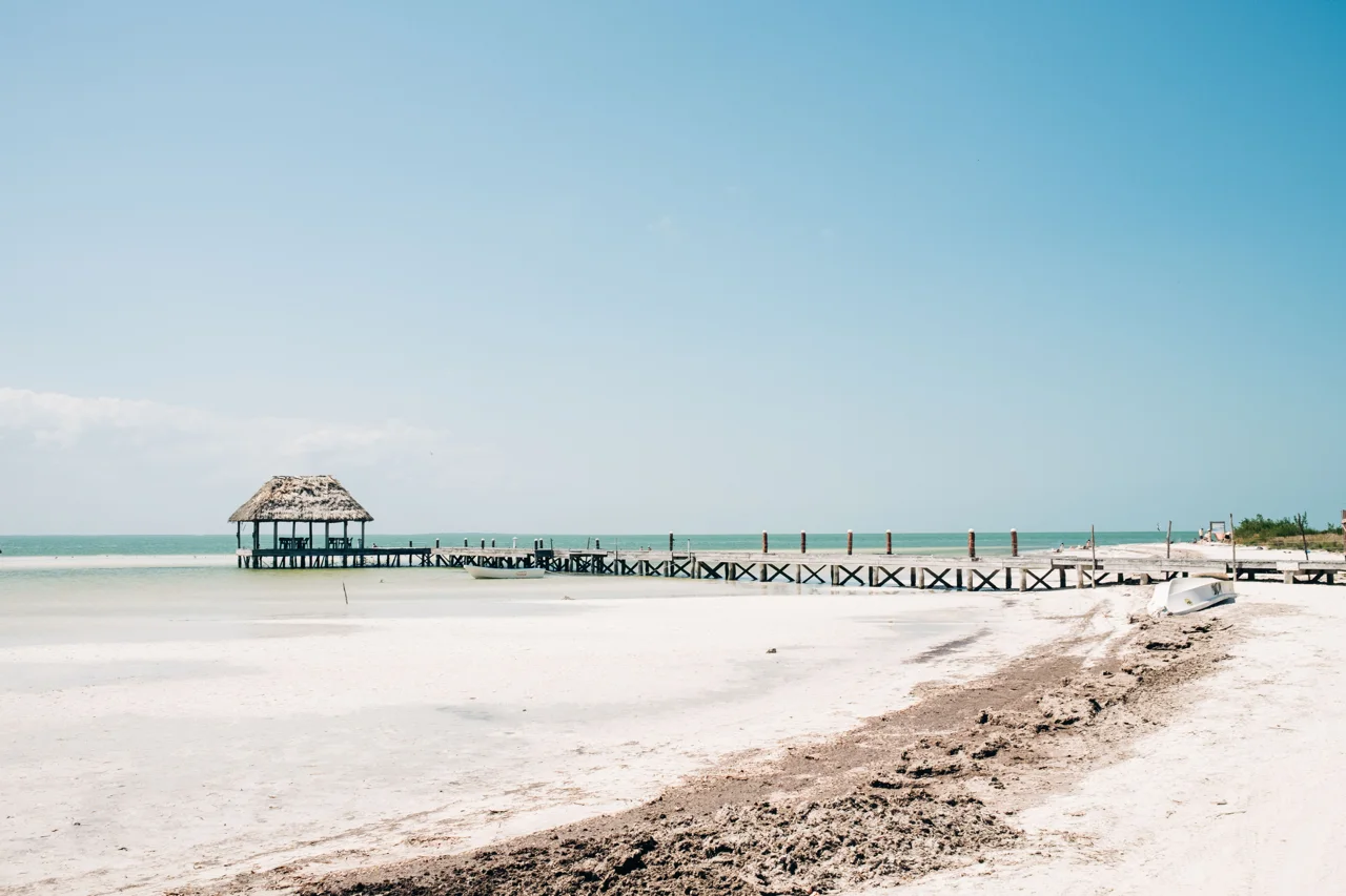 Areia branca, águas rasas e um cais de madeira na Ilha Holbox.