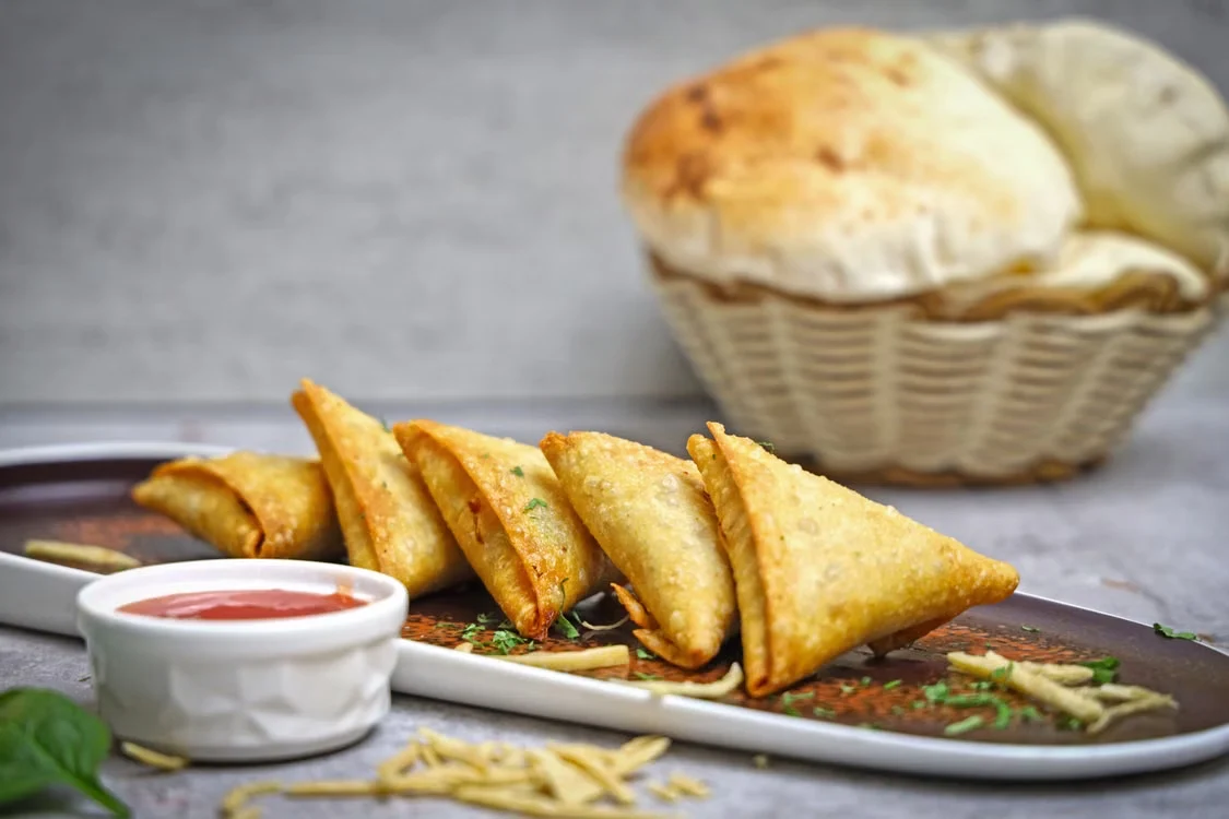Golden samosas on a platter with dipping sauce