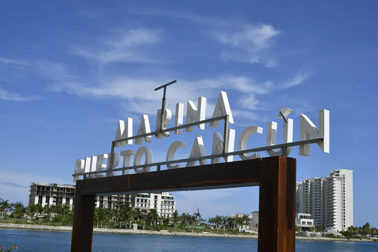 Placa da Marina Puerto Cancun à beira-mar com prédios residenciais ao fundo.
