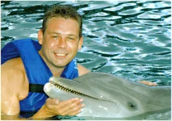 A man in a life jacket beside a dolphin in the water