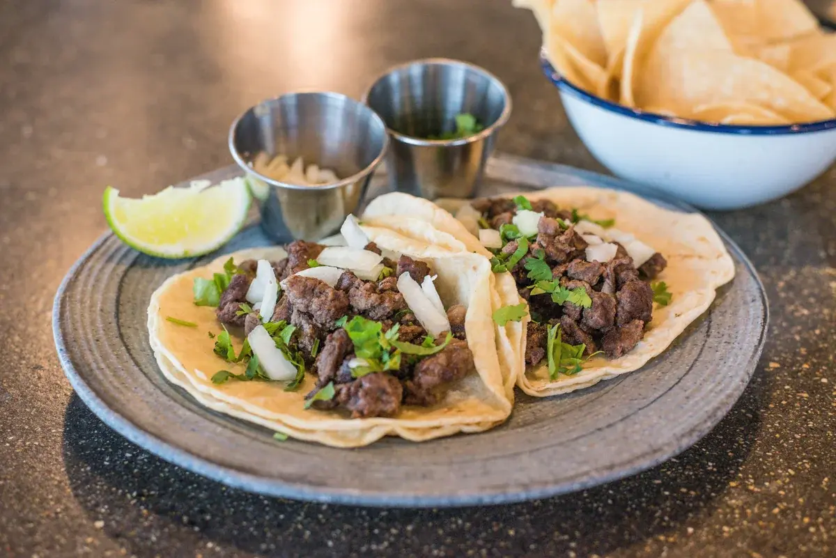 Two tacos topped with onion and cilantro beside a lime wedge