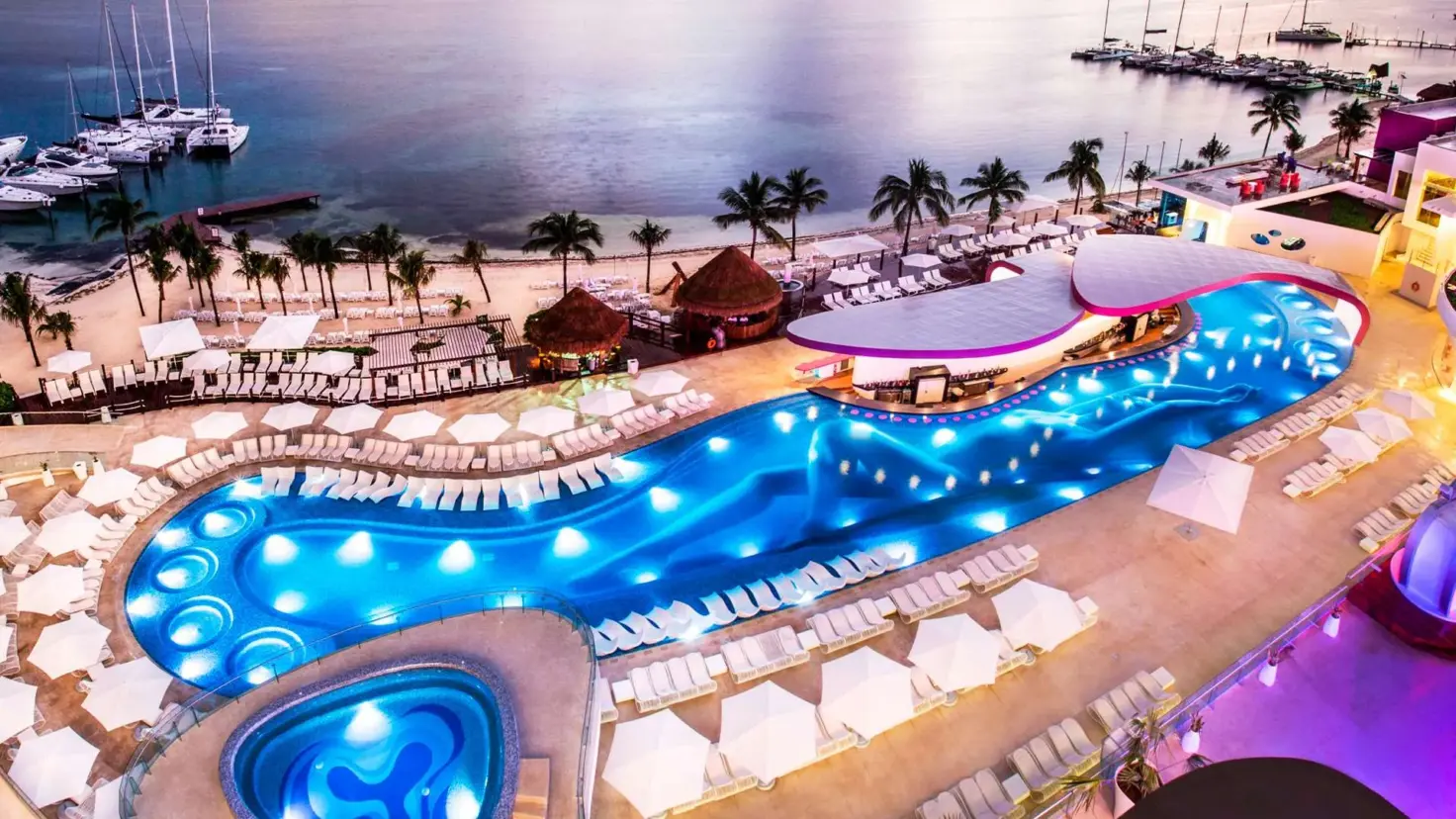 Evening aerial view of the Sexy Pool and curved Boost swim-up bar beside the beach at Temptation Cancun Resort
