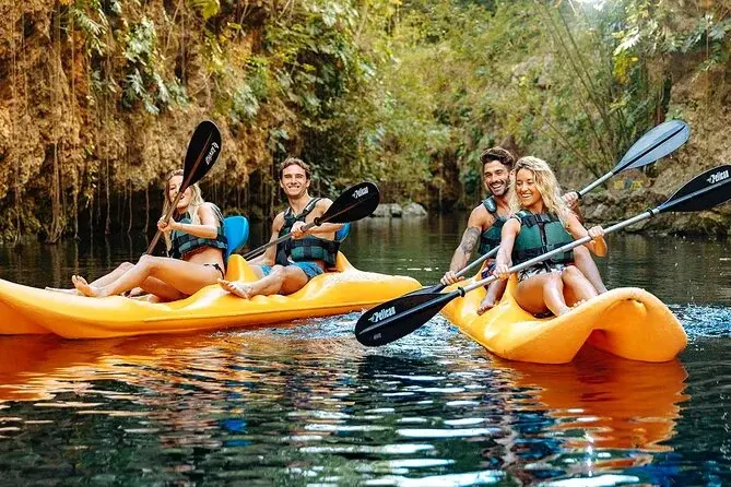 Visitors kayaking on a jungle-lined cenote during Xenotes