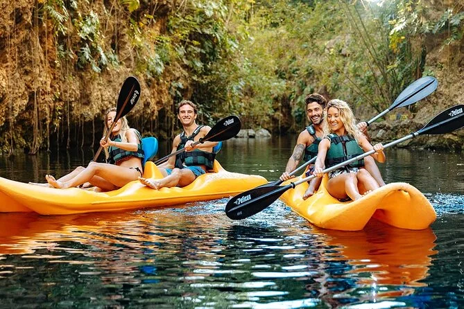 Visitors kayaking on a jungle-lined cenote during Xenotes