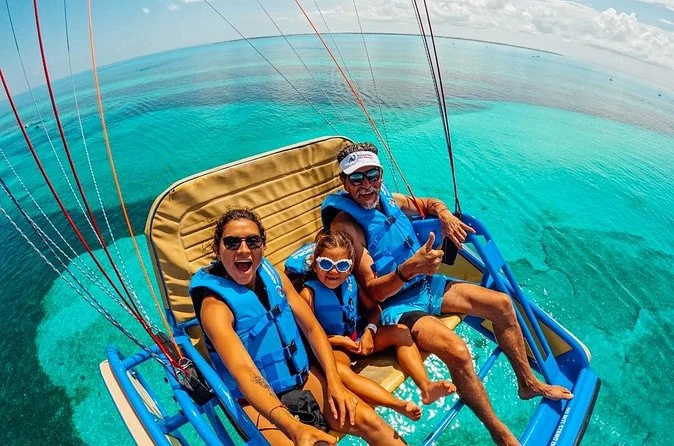 Guests wearing life jackets in a suspended Skyrider parasailing seat above turquoise water