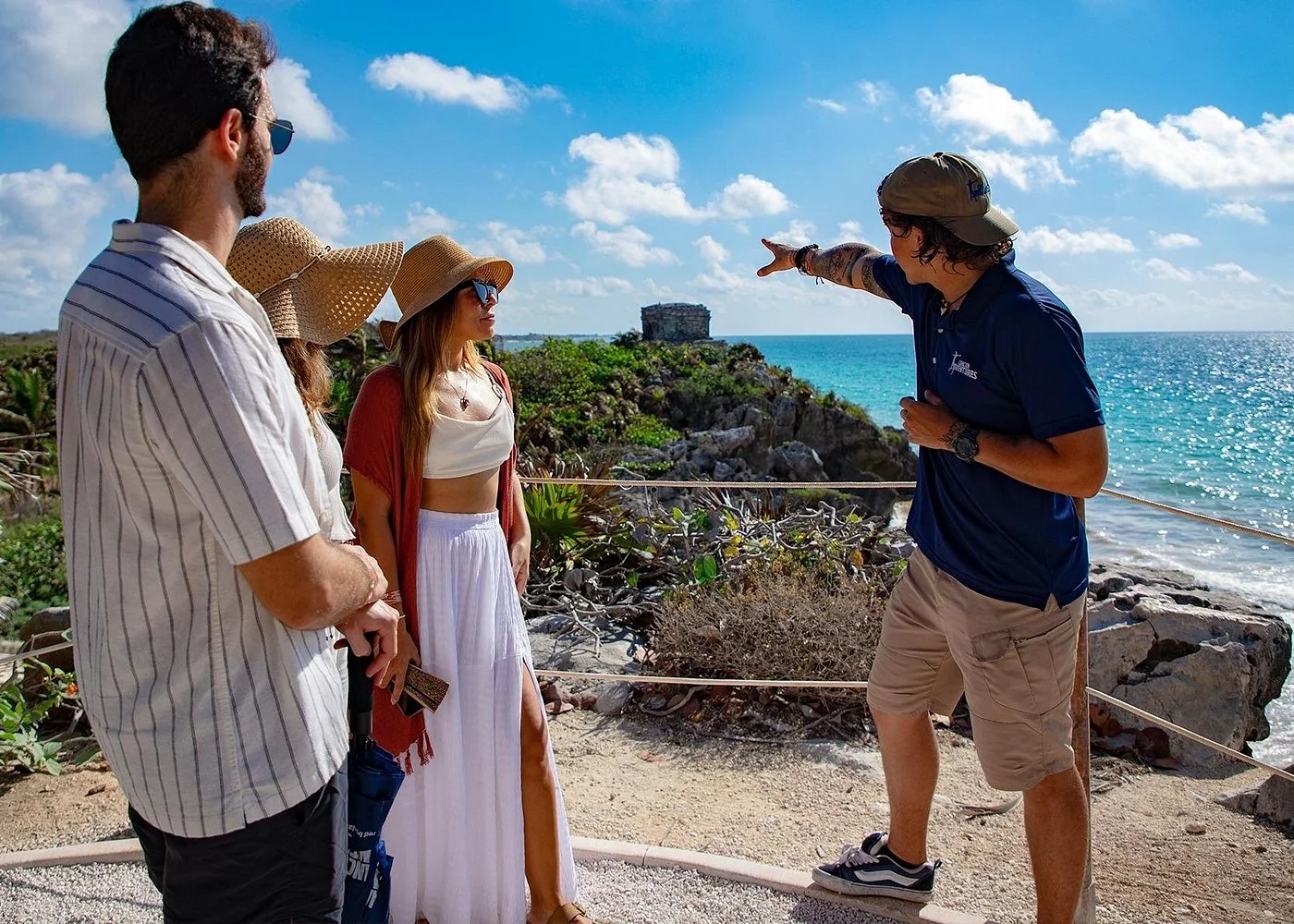 Guide explaining the coastal ruins at Tulum to visitors beside the Caribbean Sea