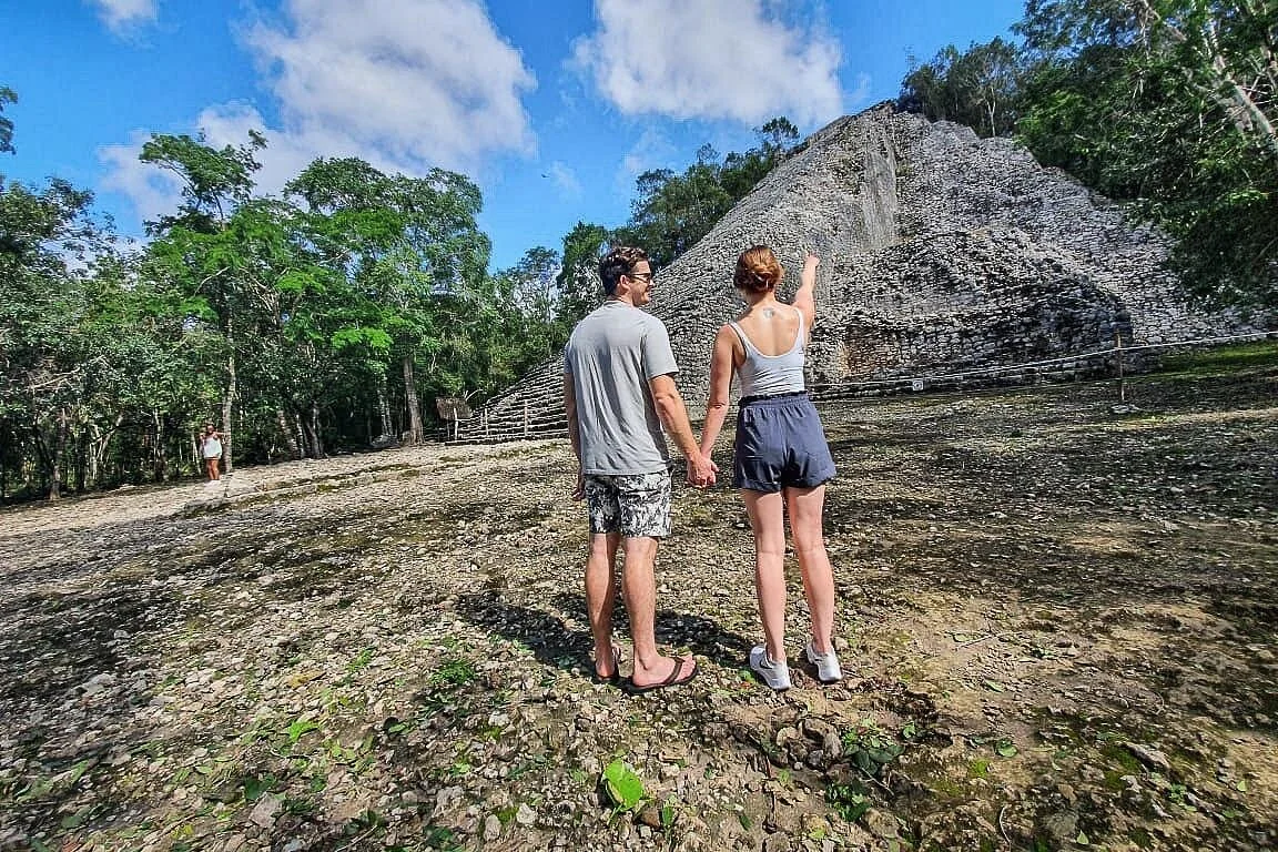 Visitors beside a stone pyramid and woodland at Cobá