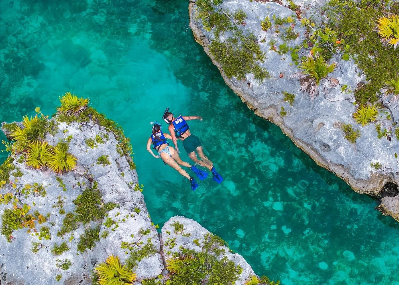 Two visitors snorkeling in a turquoise Xel-Há inlet between rocky banks