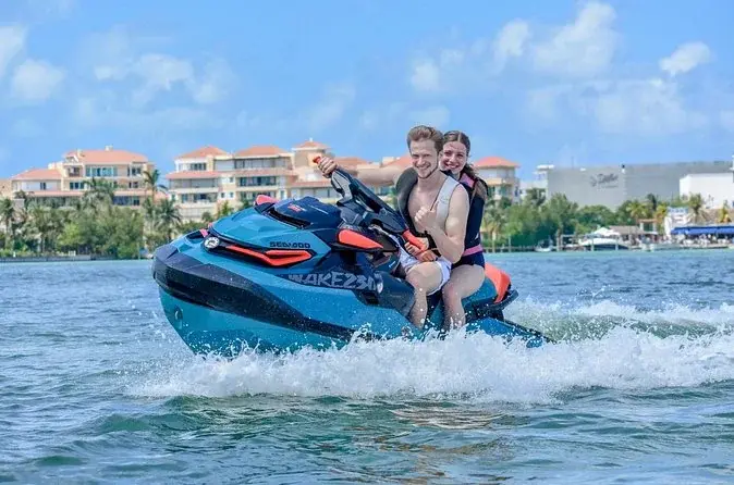 Two riders on a jet ski with Cancun waterfront hotels behind them